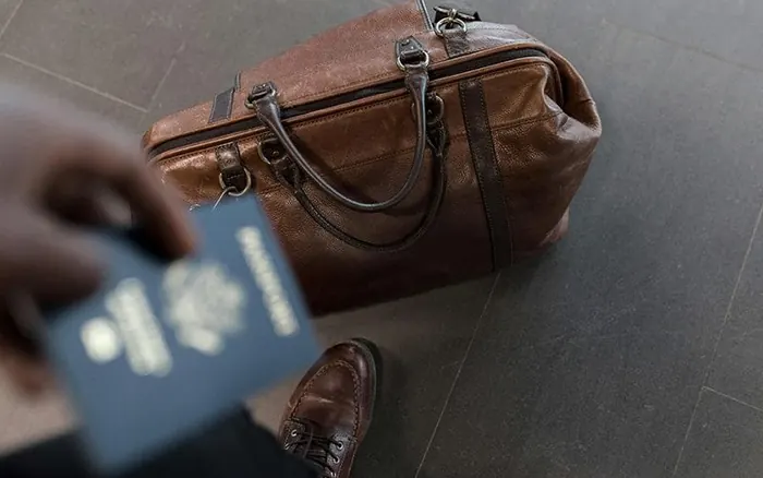 person holding passport with brown travel bag on floor