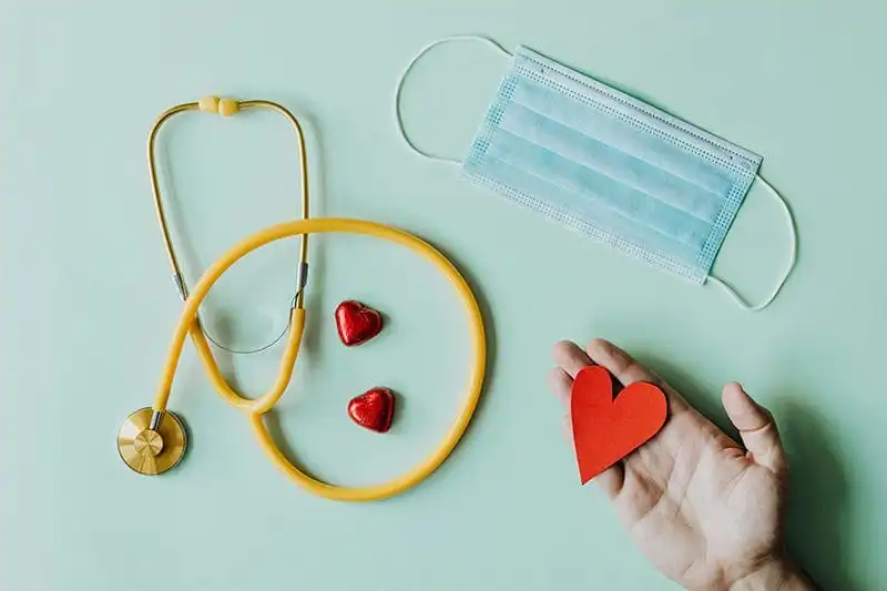 stethoscope, hand holding a heart, and a mask